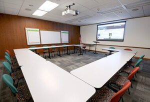 U-shaped meeting room with white tables, colorful chairs, wood paneling, and a projector showing "UA Archives".